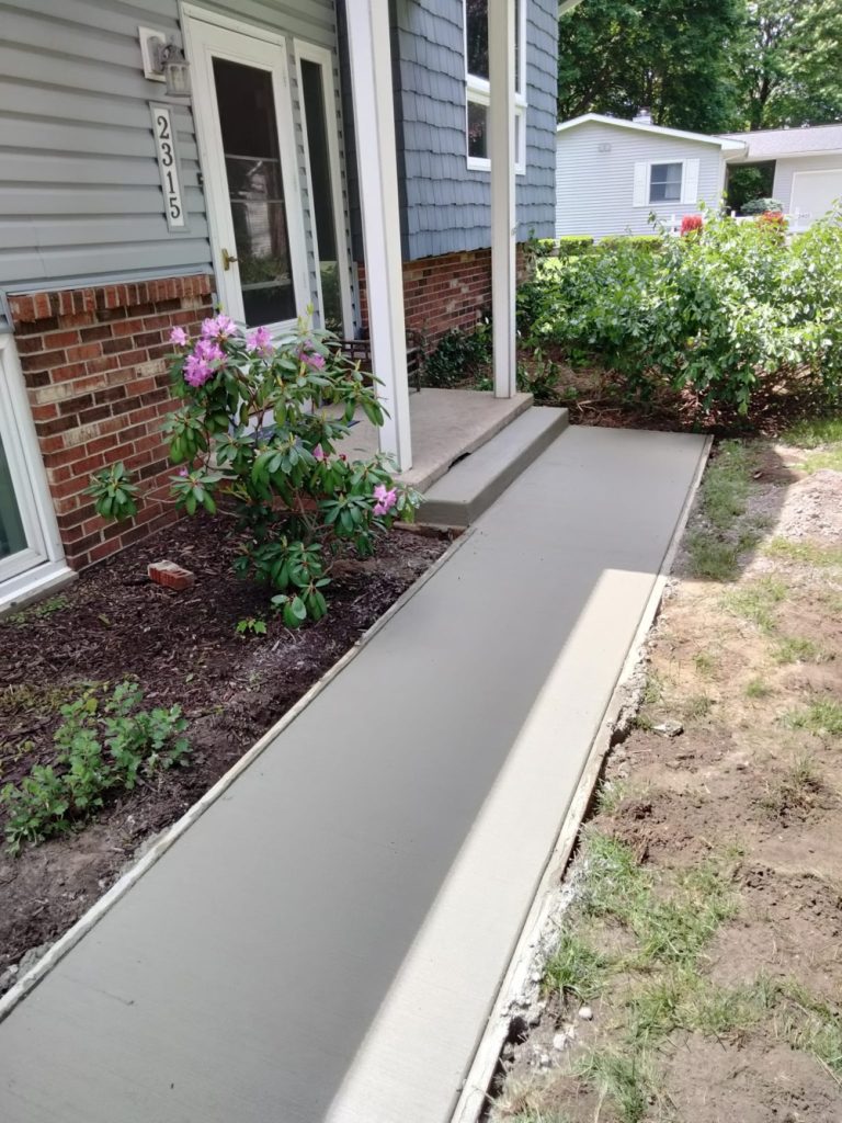 New concrete sidewalk leading up to a front porch patio.